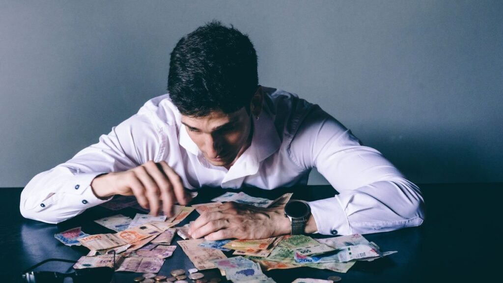 Homem debruçado sobre notas de dinheiro espalhadas na mesa, com expressão de preocupação